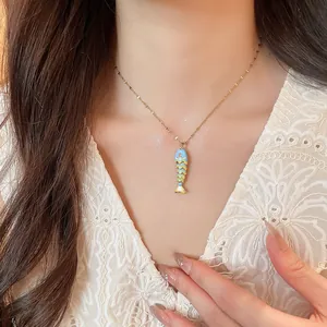 Close-up of a colorful fish pendant necklace on a gold chain worn by a woman.