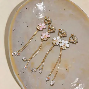 Detail of elegant floral tassel clip earrings with pink and white petals and gold finish.