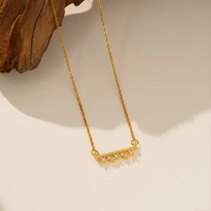 Primer plano detallado de un collar de barra de acero de titanio dorado con piedras de circón