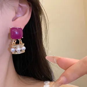 Detailansicht eines goldenen Vintage-Ohrrings mit lila Stein, Perlen und glänzenden Strasssteinen.