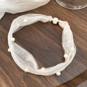 Close-up of white mesh choker with embedded pearls and magnetic rhinestone clasp