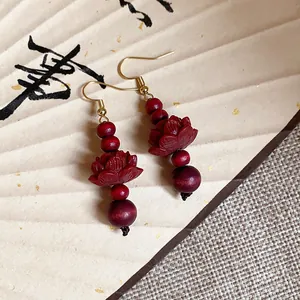 Detail of retro Chinese style wooden lotus drop earrings with red beads and gold hooks.
