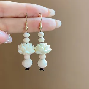 Macro view showing the intricate carved white lotus flower and wood beads on drop earrings.