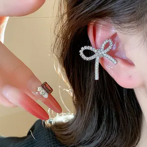 Close-up of sparkling zircon bow ear cuff on ear cartilage with elegant warm lighting