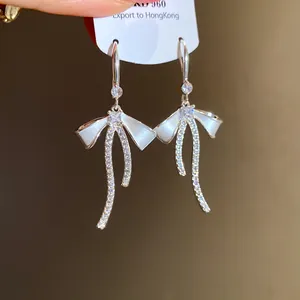 Detailed view of silver bow earrings featuring sparkling zircons and a white enamel finish.