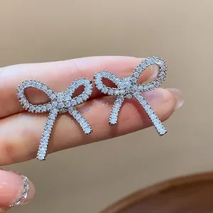 Close-up macro view of exquisite shimmering zirconia bow ear clips held between fingers