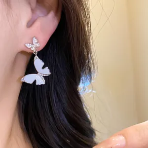 Close-up of elegant butterfly drop earrings with zircons and white enamel detail.