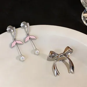 Dettaglio di orecchini a clip a coda di pesce in smalto rosa con perle e fiocco argento