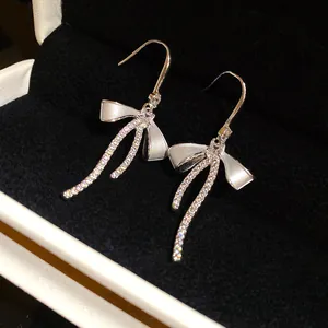 Close-up of elegant silver bow earrings with zircon stones and white enamel details