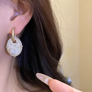 Detailansicht eines ovalen Zirkon- und Süßwasserperlen-Ohrrings am Ohr einer Person.