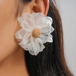 Close-up detail of a handmade white chiffon flower earring with a natural raffia center.