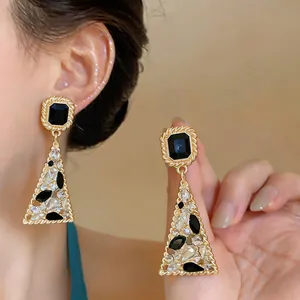 Dettaglio di orecchini d'oro geometrici vintage con pietre nere e cristalli brillanti
