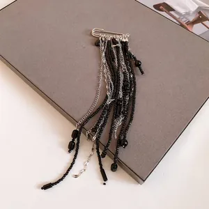 Detailed macro view of a silver safety pin brooch with long black beaded tassels