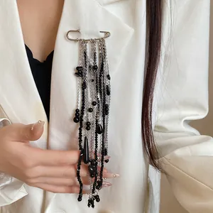 Detailed view of safety pin brooch with long black bead tassels on white blazer