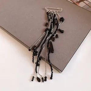 Close-up detail of a silver safety pin brooch featuring long black beaded chain tassels