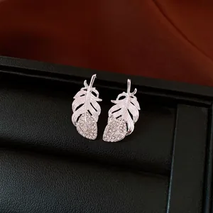 Close-up of silver-toned feather stud earrings with sparkling rhinestones on black tray.