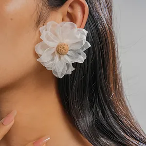 Detailed macro view of a white chiffon mesh flower earring with raffia center on a model's ear