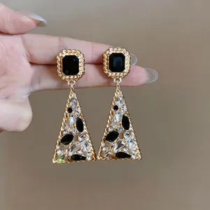 Dettaglio di orecchini a goccia triangolari vintage in oro con strass neri e trasparenti