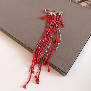 Close-up detail of a vintage paperclip brooch with long red bead and silver chain tassels.