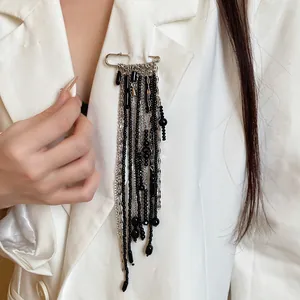 Detailed view of a vintage safety pin brooch with long black bead tassels on a white blazer.
