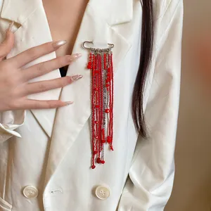 Close-up detail of a silver paperclip brooch with elegant long red beaded tassels.