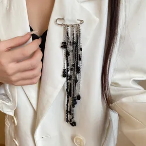 Detail of a vintage silver safety pin brooch with long black beaded tassels on a white blazer.