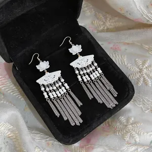 Detail shot of Chinese style fan-shaped earrings with long silver tassels and white flowers.
