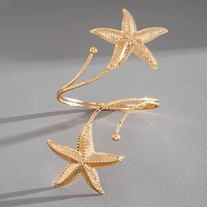 Detail shot of a golden metallic starfish arm cuff with a textured finish on grey background