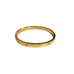 Elegant gold bangle bracelet featuring heart engravings and sparkling zircon stones