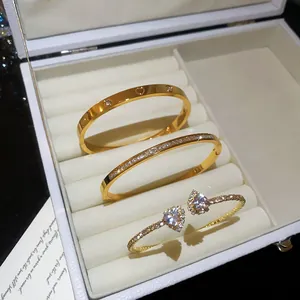 Close-up of three elegant gold-tone bangles with zircon heart details in a white jewelry box