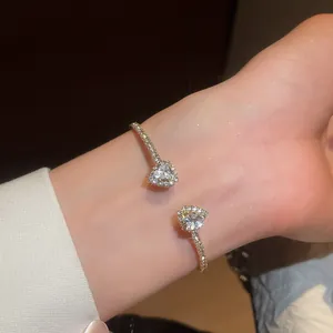 Elegant gold open bangle featuring sparkling heart-shaped cubic zirconia on a wrist.