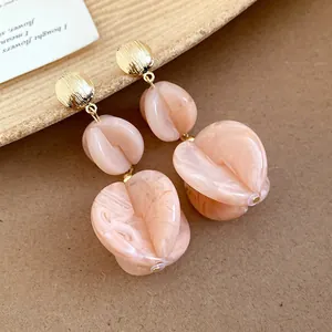 Close-up of elegant peach acrylic drop earrings with gold studs on a textured background