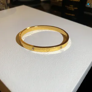 Close-up of gold-plated bangle featuring engraved heart patterns and zircon accents
