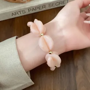 Detail of peach acrylic shell-shaped bead bracelet with gold accents worn on a wrist