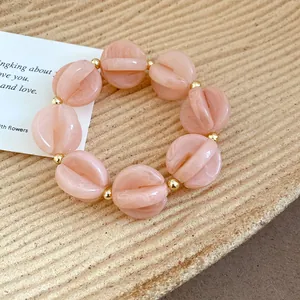 Detail view of pink acrylic bead bracelet with golden accents on textured plate