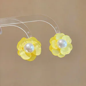 Close-up of yellow flower stud earrings with pearl centers on transparent display stand