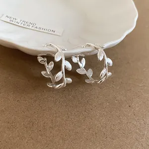 Detail view of silver brushed metal C-shaped branch earrings with delicate leaf design.