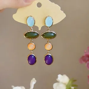 Close-up of elegant resin oval earrings with multi-colored stones and gold trim