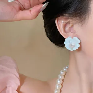 Detailed close-up of an elegant white flower stud earring with a pearl worn by a model