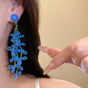 Close-up of blue glass bead floral tassel earrings worn on ear with silver needle