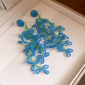 Detailed view of handcrafted blue and green beaded flower tassel earrings in jewelry box