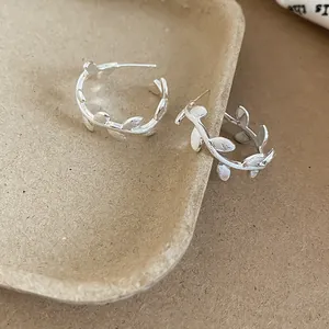 Macro view of C-shaped branch earrings showing delicate brushed metal leaf texture