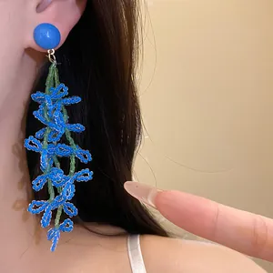 Detailed close-up of blue glass flower tassel earrings with green bead strings on model