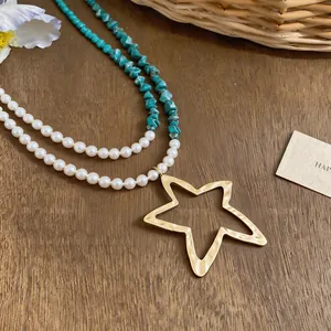Detalle de collar multicapa con perlas, piedras turquesas y colgante de estrella dorada.