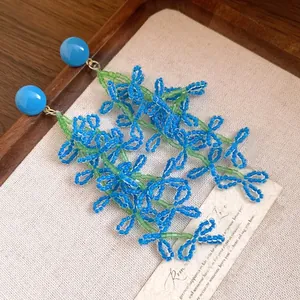Macro view of blue and green beaded glass flower tassel earrings with silver needles