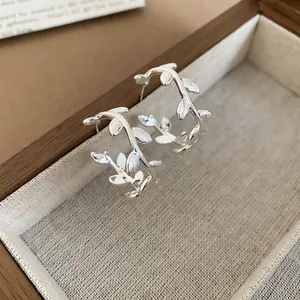 Close-up of matte silver branch hoop earrings featuring a brushed metal texture on linen.
