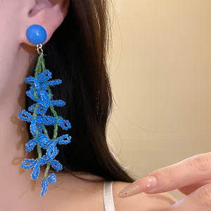 Detailed view of handmade blue and green beaded floral tassel earrings worn by model