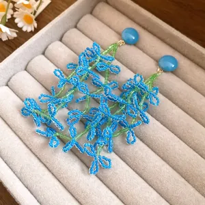 Detailed close-up view of elegant blue and green beaded flower tassel earrings on grey tray