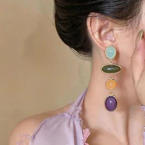 Detail view of elegant multi-color resin oval dangling earrings worn by a model on ear