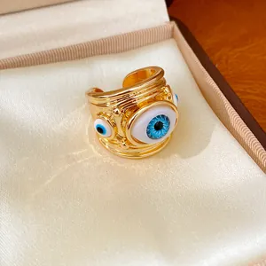 Macro detail of a golden adjustable ring featuring blue resin Evil Eye charms